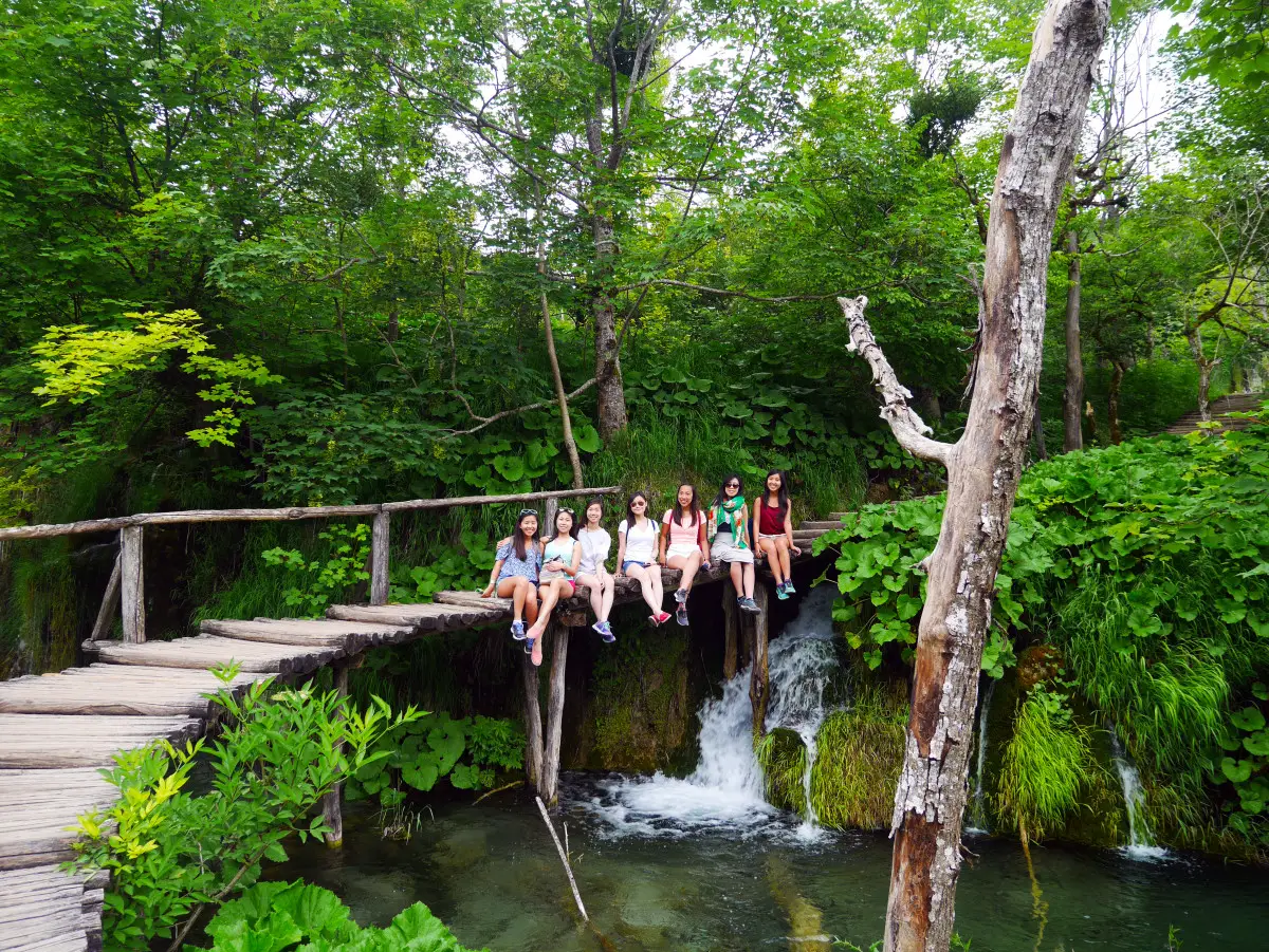 Our travel group sitting on a wooden bridge on top of a waterfall at Plitvice National Park, Croatia| Laugh Travel Eat
