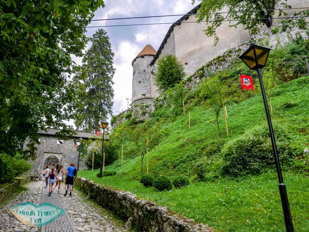 Cobble-stone-path-with-flags-on-lamppost-leading-to-Castle-Bled-Slovenia-laugh-travel-eat