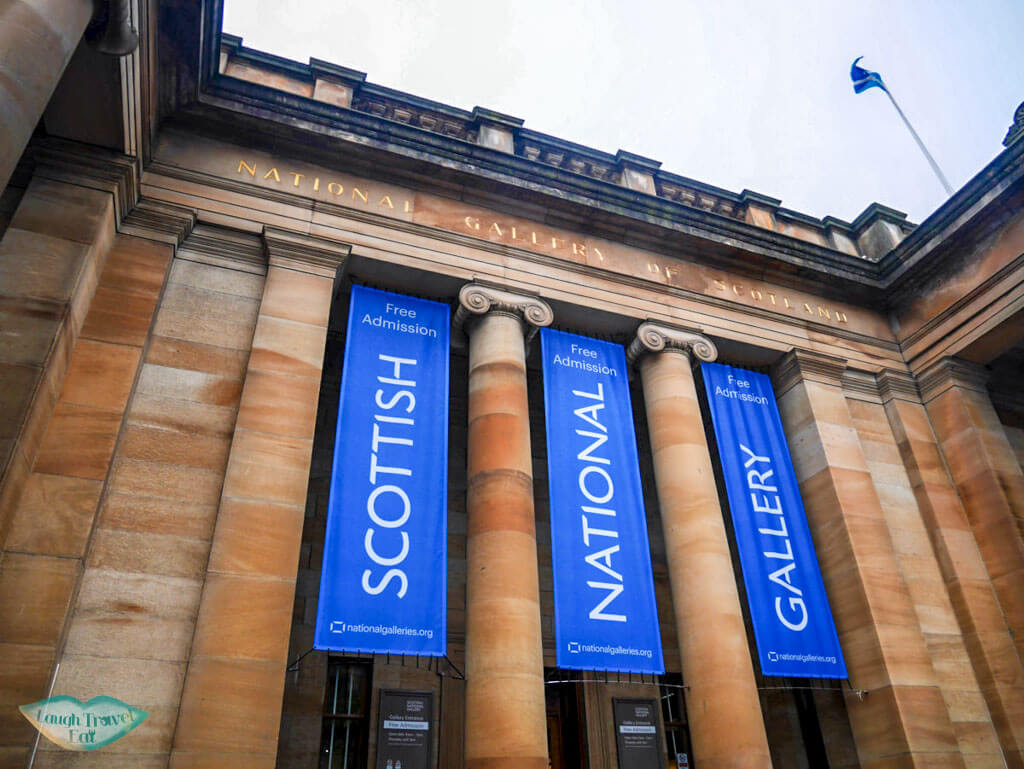 Neoclassical building with blue banners of the Scottish National Gallery - Laugh Travel Eat